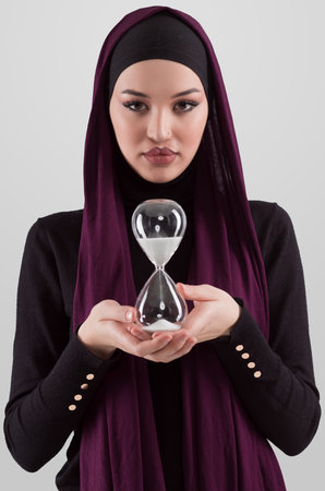 Beautiful arab businesswoman wearing hijab and holding sand clock. Time is passing and its a...