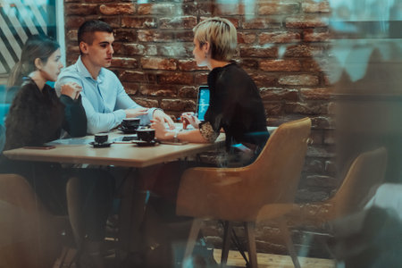 Photo through the glass of a group of business people sitting in a cafe and discussing business plans and ideas for new online commercial servicesの写真素材