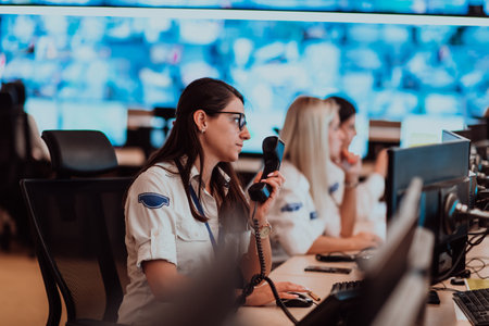 Group of Security data center operators working in a CCTV monitoring room looking on multiple monitors.Officers Monitoring Multiple Screens for Suspicious Activitiesの写真素材