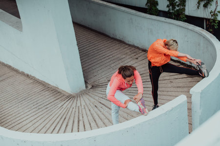 Two women warming up together and preparing for a morning run in an urban environment. Selective focusの写真素材