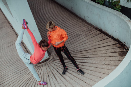 Two women warming up together and preparing for a morning run in an urban environment. Selective...
