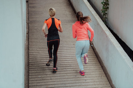 Two women in sports clothes running in a modern urban environment. The concept of a sporty and...