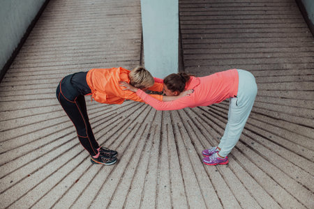 Two women warming up together and preparing for a morning run in an urban environment. Selective...