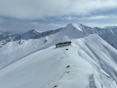 Cinematic Aerial Epic scene of group of skiers and snowboarders on top of a mountain. Winter at the summit peak or top with a group of freeride or backcountry skiers.の写真素材