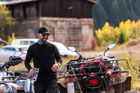 A man in a forest posing next to a quad and preparing for rideの写真素材
