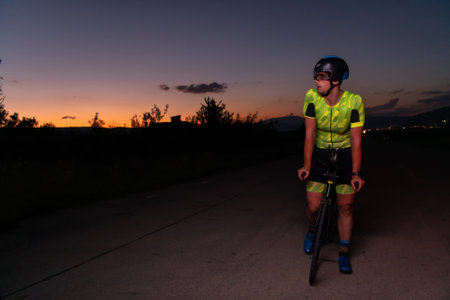 A triathlete rides his bike in the darkness of night, pushing himself to prepare for a marathon. The contrast between the darkness and the light of his bike creates a sense of drama and highlights the athletes determination and perseverance.の写真素材