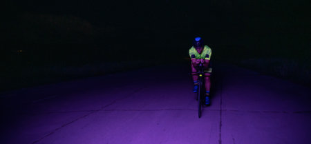 A triathlete rides his bike in the darkness of night, pushing himself to prepare for a marathon. The contrast between the darkness and the light of his bike creates a sense of drama and highlights the athletes determination and perseverance.の写真素材