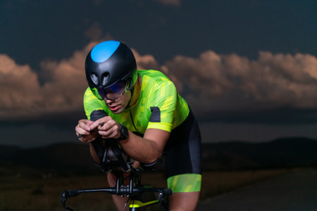 A triathlete rides his bike in the darkness of night, pushing himself to prepare for a marathon. The contrast between the darkness and the light of his bike creates a sense of drama and highlights the athletes determination and perseverance.の写真素材