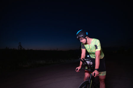 A triathlete resting on the road after a tough bike ride in the dark night, leaning on his bike in complete exhaustionの写真素材