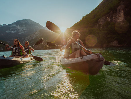 A group of friends enjoying fun and kayaking exploring the calm river, surrounding forest and large natural river canyons during an idyllic sunset.の写真素材