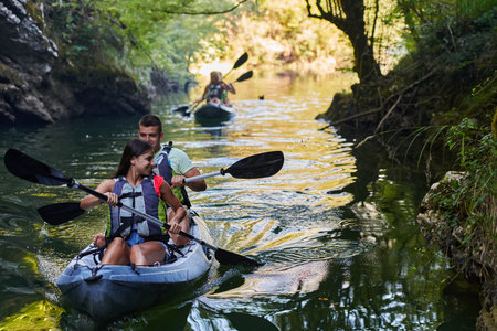 A group of friends enjoying having fun and kayaking while exploring the calm river, surrounding forest and large natural river canyonsの写真素材