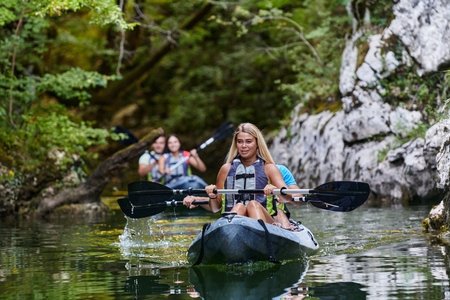 A group of friends enjoying having fun and kayaking while exploring the calm river, surrounding forest and large natural river canyonsの写真素材
