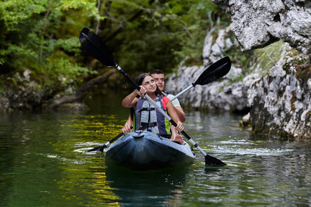 A young couple enjoying an idyllic kayak ride in the middle of a beautiful river surrounded by forest greeneryの写真素材