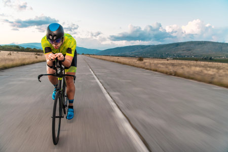 Triathlete riding his bicycle during sunset, preparing for a marathon. The warm colors of the sky provide a beautiful backdrop for his determined and focused effort.の写真素材