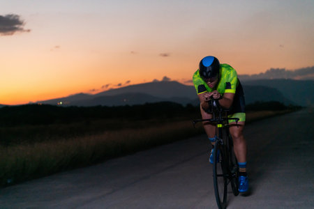 A triathlete rides his bike in the darkness of night, pushing himself to prepare for a marathon. The contrast between the darkness and the light of his bike creates a sense of drama and highlights the athletes determination and perseverance.の写真素材