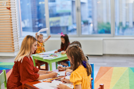 Creative kids during an art class in a daycare center or elementary school classroom drawing with female teacher.の写真素材