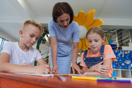 Creative kids during an art class in a daycare center or elementary school classroom drawing with female teacher.の写真素材