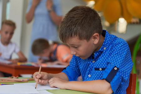 A boy at a preschool institution sits and draws in a notebook with a smile on his faceの写真素材