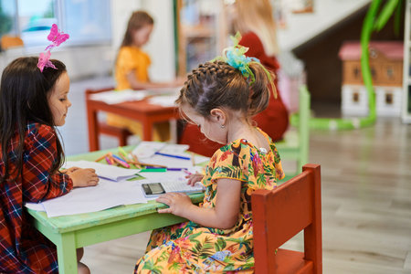 Creative kids during an art class in a daycare center or elementary school classroom drawing with...
