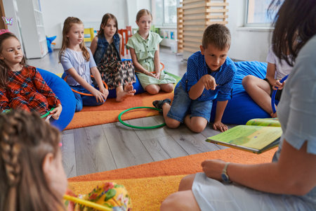 A happy female teacher sitting and playing hand games with a group of little schoolchildrenの写真素材