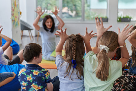 A happy female teacher sitting and playing hand games with a group of little schoolchildrenの写真素材