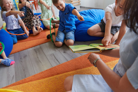 A happy female teacher sitting and playing hand games with a group of little schoolchildrenの写真素材