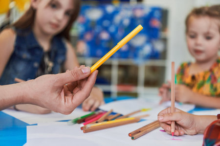 Close up photo of kids during an art class in a daycare center or elementary school classroom drawing with female teacher.の写真素材