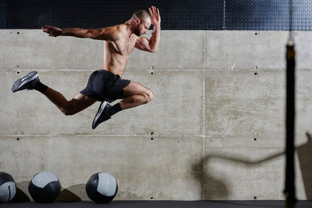 A muscular man captured in air as he jumps in a modern gym, showcasing his athleticism, power, and determination through a highintensity fitness routineの写真素材