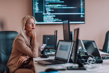 A businesswoman sitting in a programmers office surrounded by computers, showing her expertise and dedication to technology.の写真素材