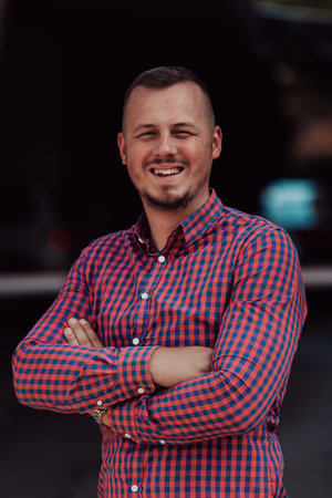 A successful young businessman in a shirt, with crossed arms, poses outdoors, confident expression...