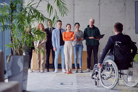 A group of diverse entrepreneurs gather in a modern office to discuss business ideas and strategies, while a colleague in a wheelchair joins them.の写真素材