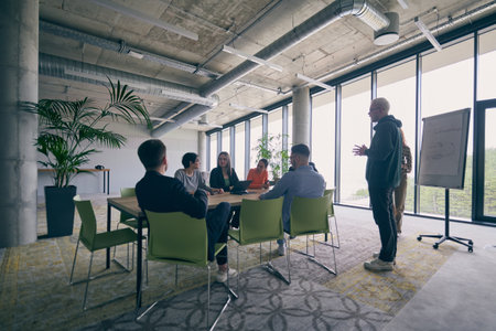 In a modern office setting, a group of business professionals attentively listens to a captivating presentation delivered by their young colleagues, showcasing their teamwork, engagement, and eagerness to learn and grow in a collaborative environment.の写真素材