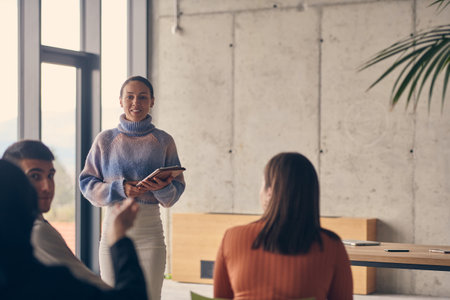A group of young business professionals in a modern office attentively listens to colleague presentation, showcasing a dynamic and collaborative atmosphere as they exchange ideas and strive for success.の写真素材