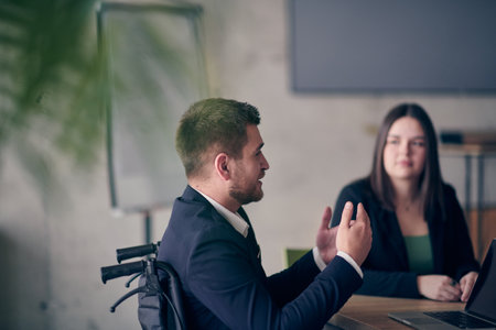 A wheelchair bound businessman confidently leads a business meeting in a large, modern office, exemplifying inclusive leadership, effective communication, and the power of diversity in driving success and achieving impactful results.の写真素材