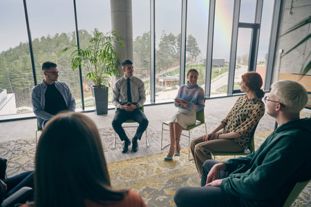 In a modern office, a diverse group of business individuals is seen gathered in a circle, engaged in...