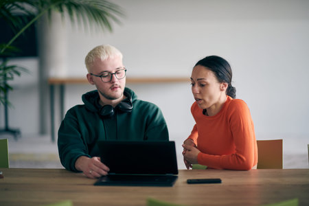 A young entrepreneurial couple sits together in a large, modern office, engaged in analyzing...