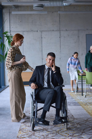 A businessman in a wheelchair and his female colleague together in a modern office, representing the...