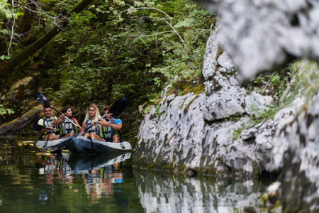 A young couple enjoying an idyllic kayak ride in the middle of a beautiful river surrounded by forest greeneryの写真素材