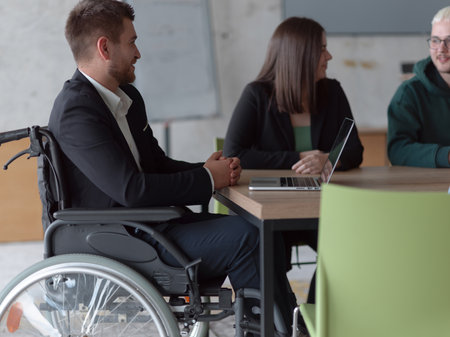 Close up photo of a diverse group of business professionals, including an person with a disability, gathered at a modern office for a productive and inclusive meeting.の写真素材