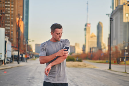 Handsome man checking his smartphone after a morning run on the vibrant streets of New York City, seamlessly blending his active lifestyle with the modern convenience of technology, as he engages with digital updates, social media, and music, immersing himself in the energetic and cosmopolitan atmosphere of the urban landscape.の写真素材