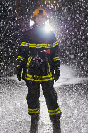 A determined female firefighter in a professional uniform striding through the dangerous, rainy night on a daring rescue mission, showcasing her unwavering bravery and commitment to saving lives.の写真素材