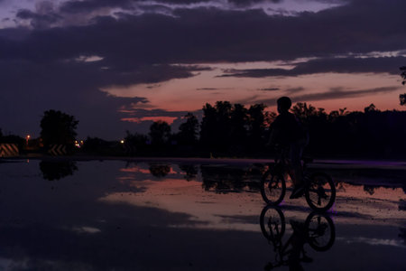 Lonely children silhouette on bike, boy riding bicycle on reflective water. Background beautiful sunset.の写真素材