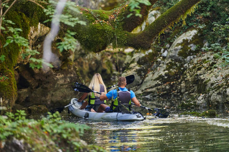 A young couple enjoying an idyllic kayak ride in the middle of a beautiful river surrounded by forest greeneryの写真素材