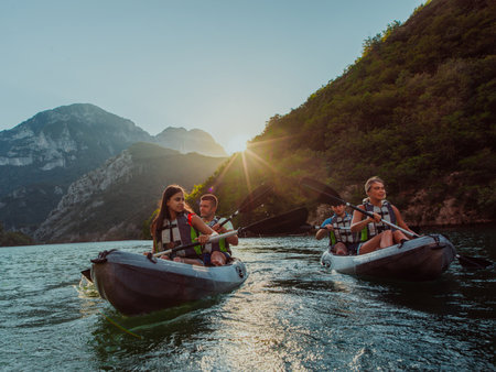 A group of friends enjoying fun and kayaking exploring the calm river, surrounding forest and large natural river canyons during an idyllic sunset.の写真素材