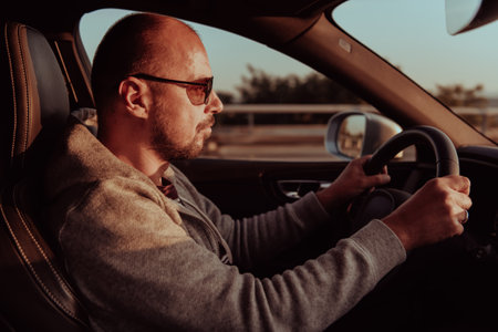 A man with a sunglasses driving a car at sunset. The concept of car travelの写真素材