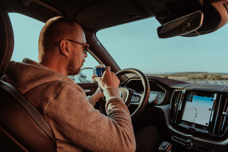 A tired man drinking acoffee while driving a car at sunset. Tired travel and long driveの写真素材