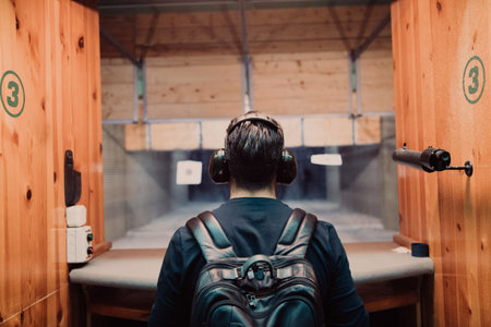 A man practices shooting a pistol in a shooting range while wearing protective headphones