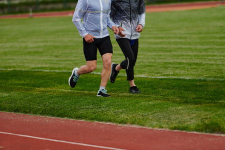 An inspiring and active elderly couple showcase their dedication to fitness as they running together on a lush green field, captured in a close-up shot of their legs in motion.の写真素材