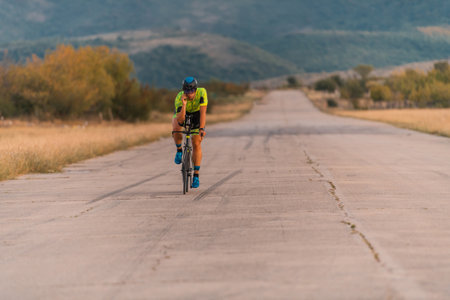 Triathlete riding his bicycle during sunset, preparing for a marathon. The warm colors of the sky provide a beautiful backdrop for his determined and focused effort.の写真素材