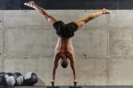 A muscular man in a handstand position, showcasing his exceptional balance and body control while...